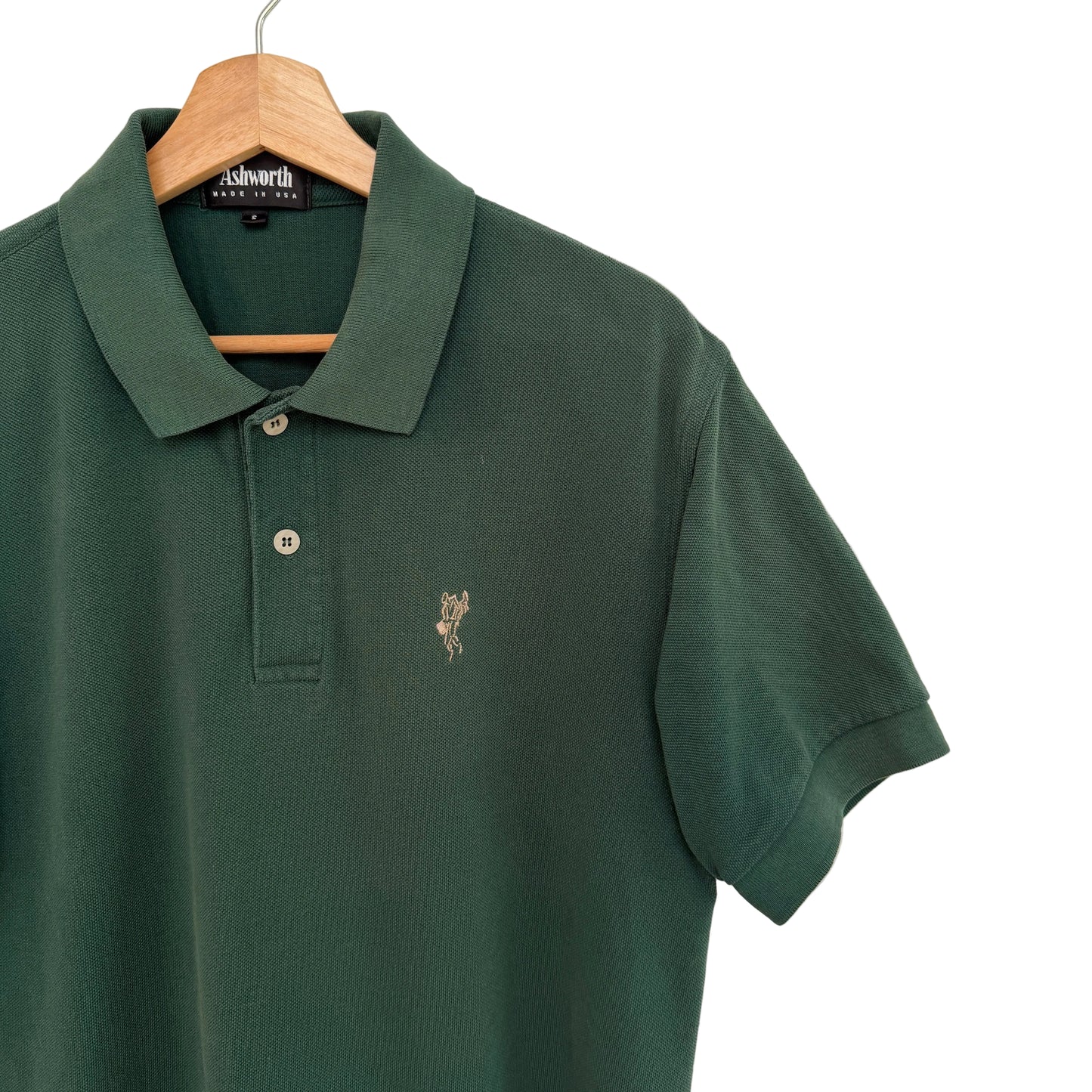 Green polo shirt with a small logo on a hanger against a white background