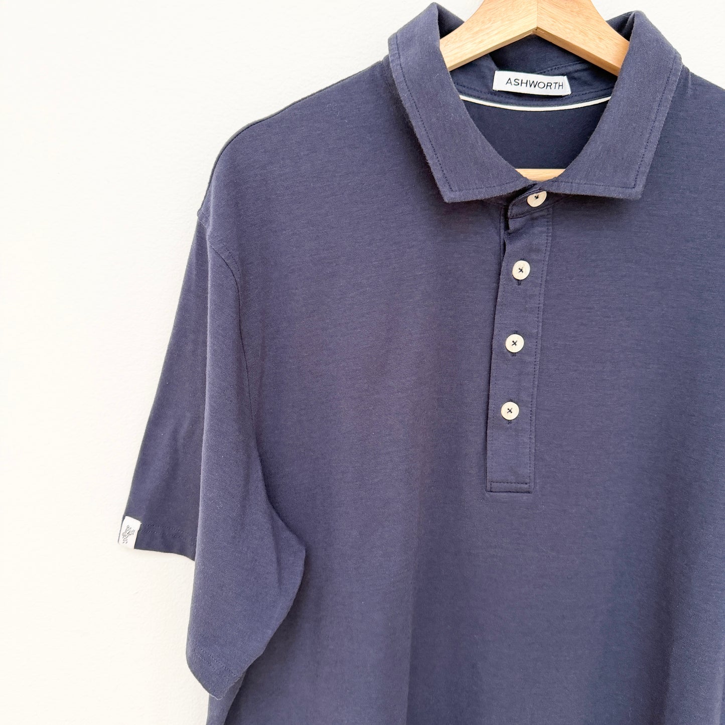 Navy blue polo shirt on a hanger with 'Ashworth' label