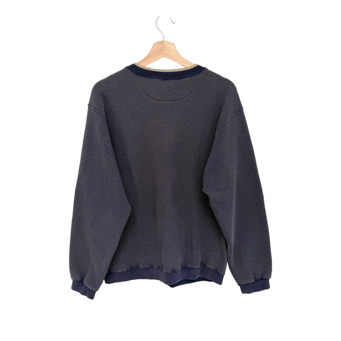 A navy crewneck sweatshirt with navy blue ribbed trim on the collar, cuffs, and hem, hanging on a wooden hanger against a plain white wall.