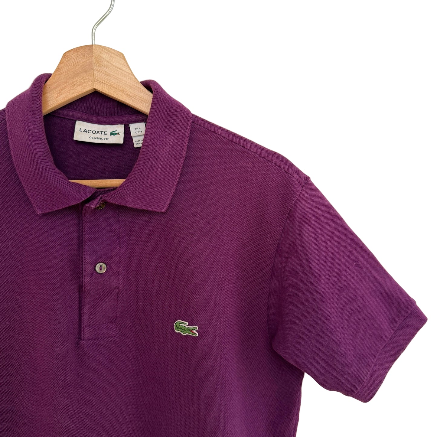 Purple polo shirt with green alligator logo on a hanger against a white background