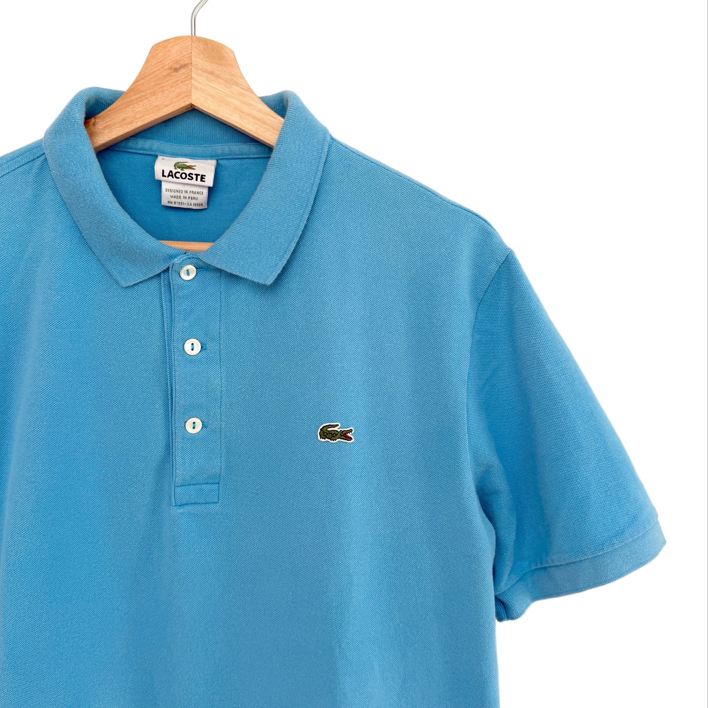 Blue polo shirt with Lacoste logo on a hanger against a white background