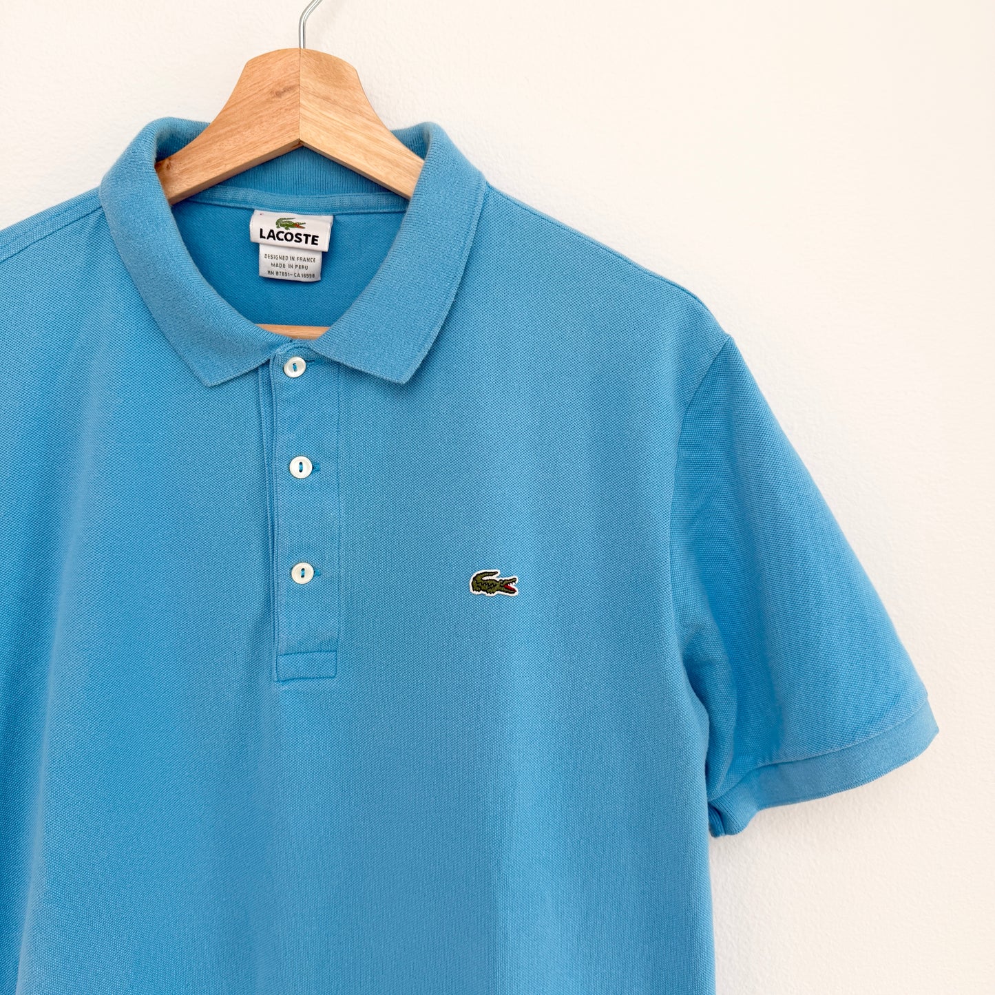 Blue polo shirt with Lacoste logo on a hanger against a white background