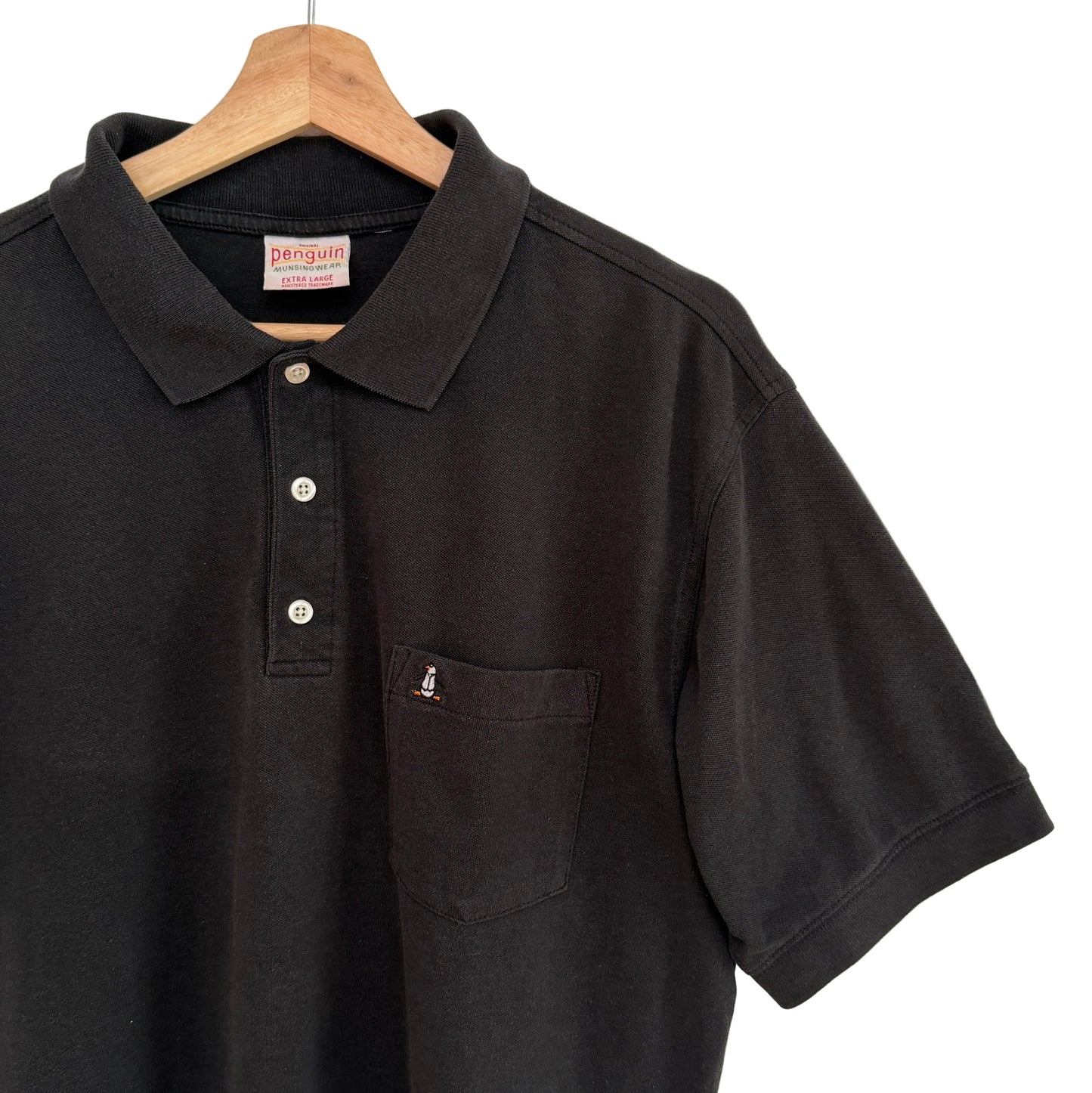 Black polo shirt with brand logo on a wooden hanger against a white background