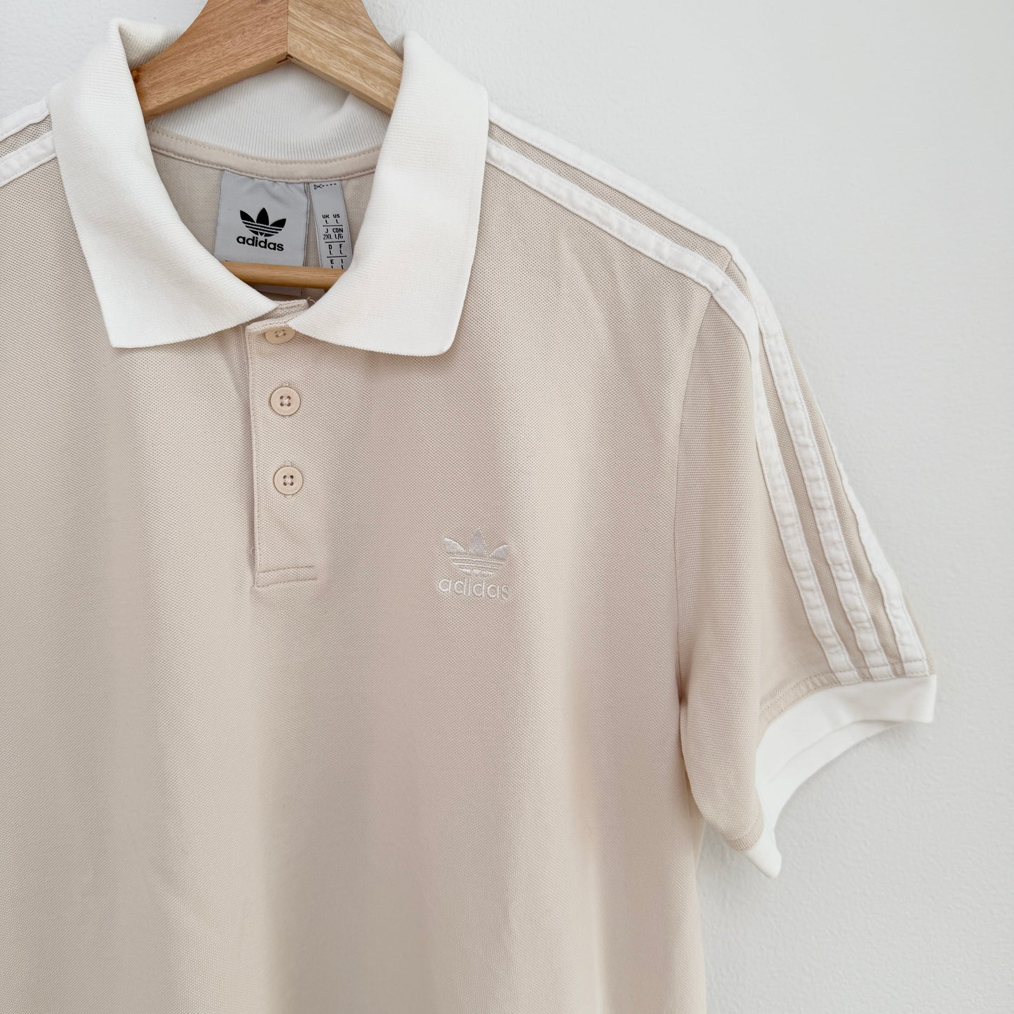 Beige polo shirt with white collar and stripes on a hanger against a light gray background