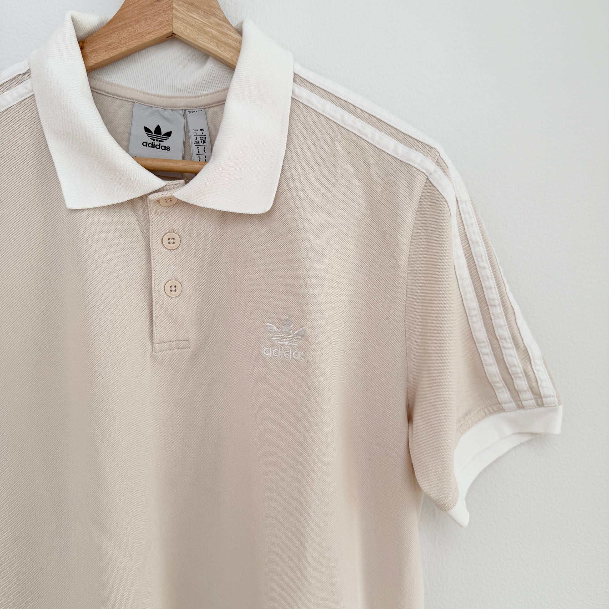 Beige polo shirt with white collar and stripes on a hanger against a light gray background