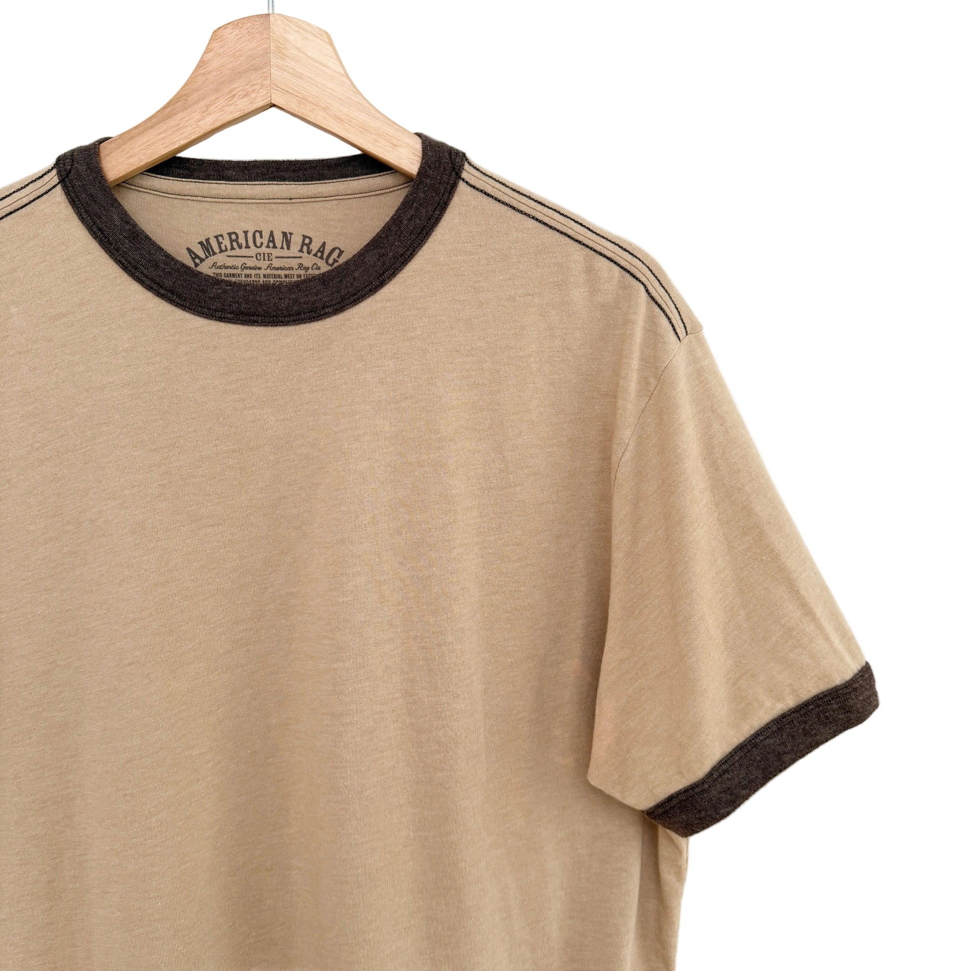 Beige t-shirt with brown trim on a hanger against a white background