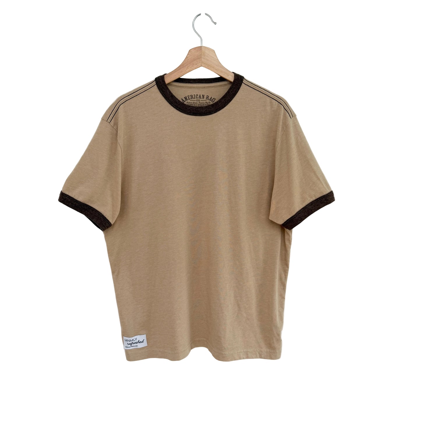 Beige t-shirt with black trim on a hanger against a white background