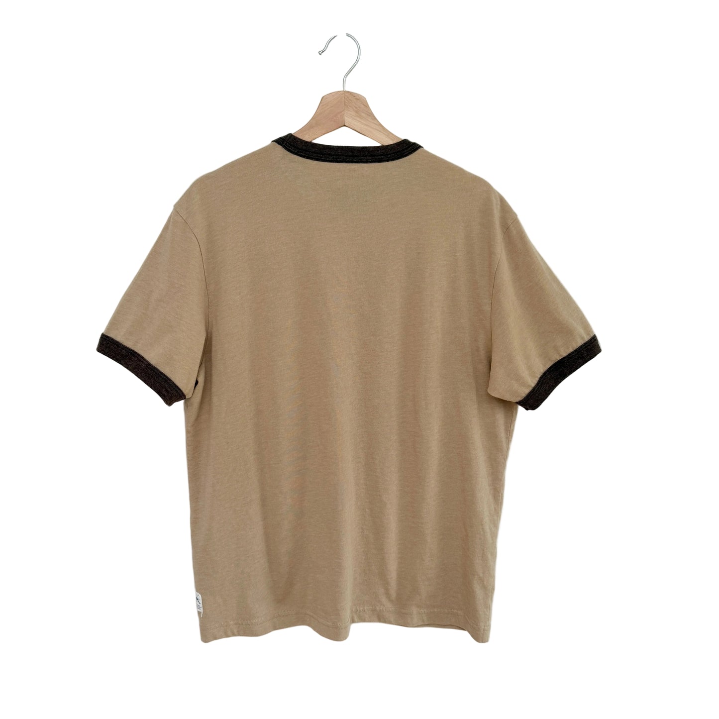 Beige t-shirt with black trim on a hanger against a white background