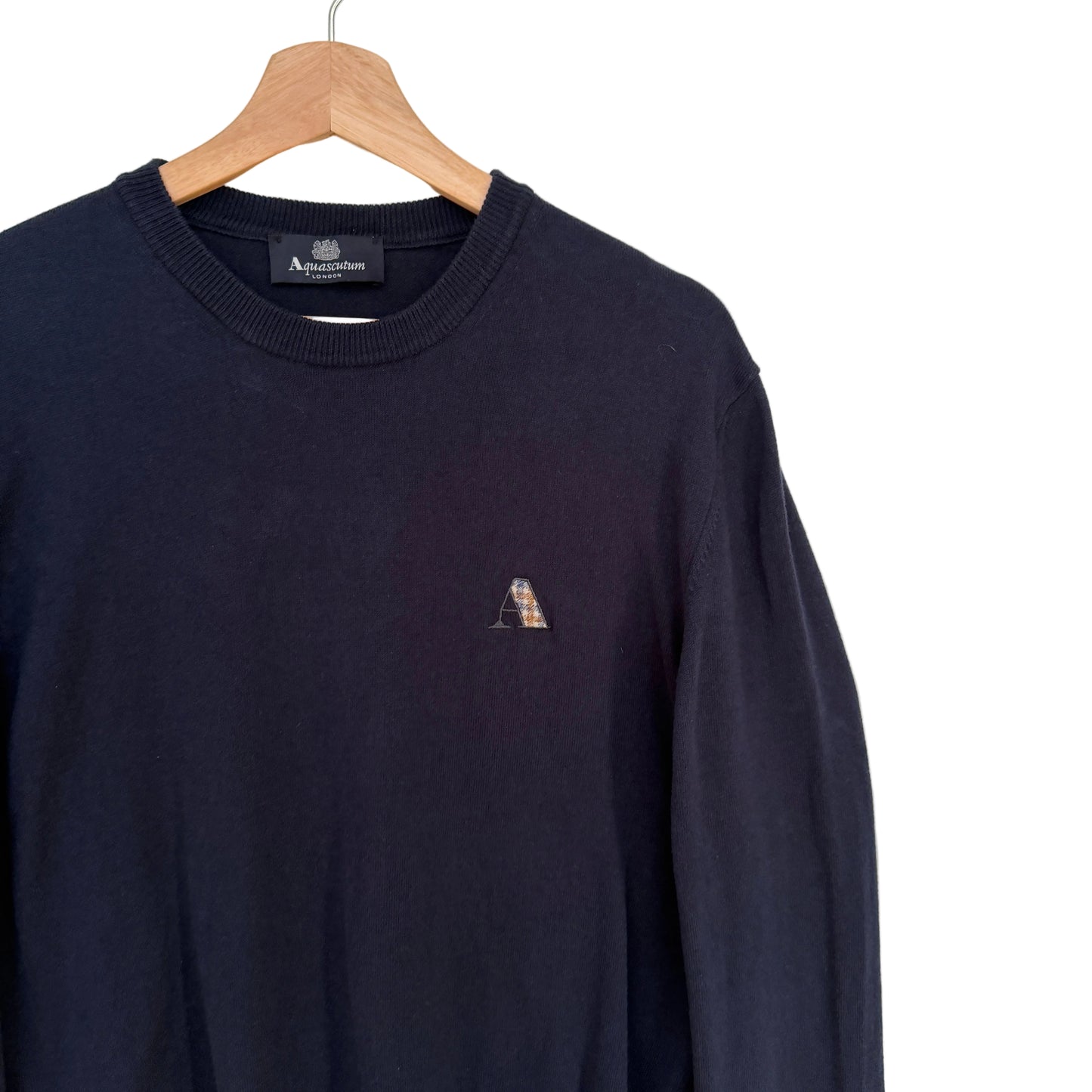 Navy blue sweater with a small logo on a hanger against a white background