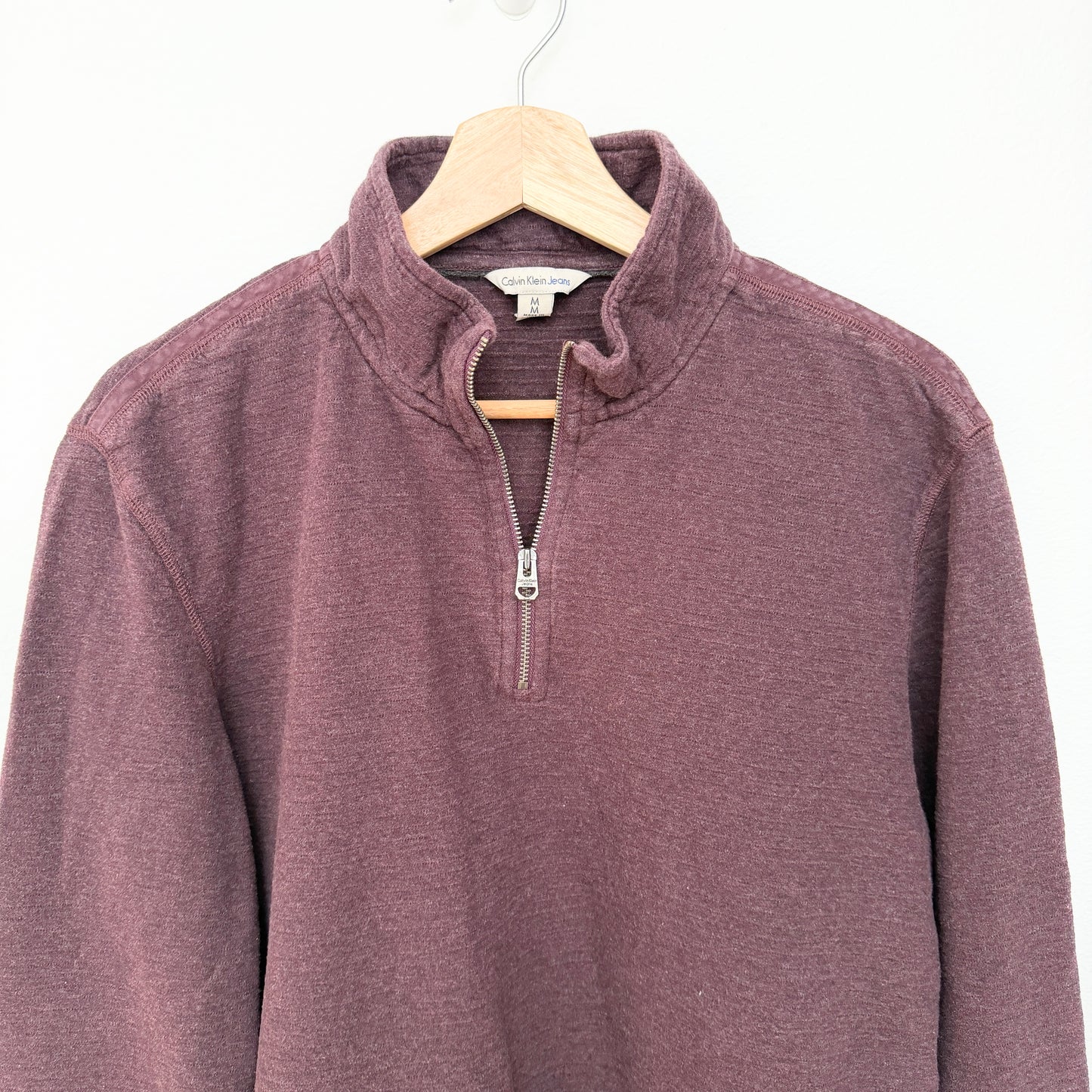 Burgundy knit pullover on a wooden hanger against a white background