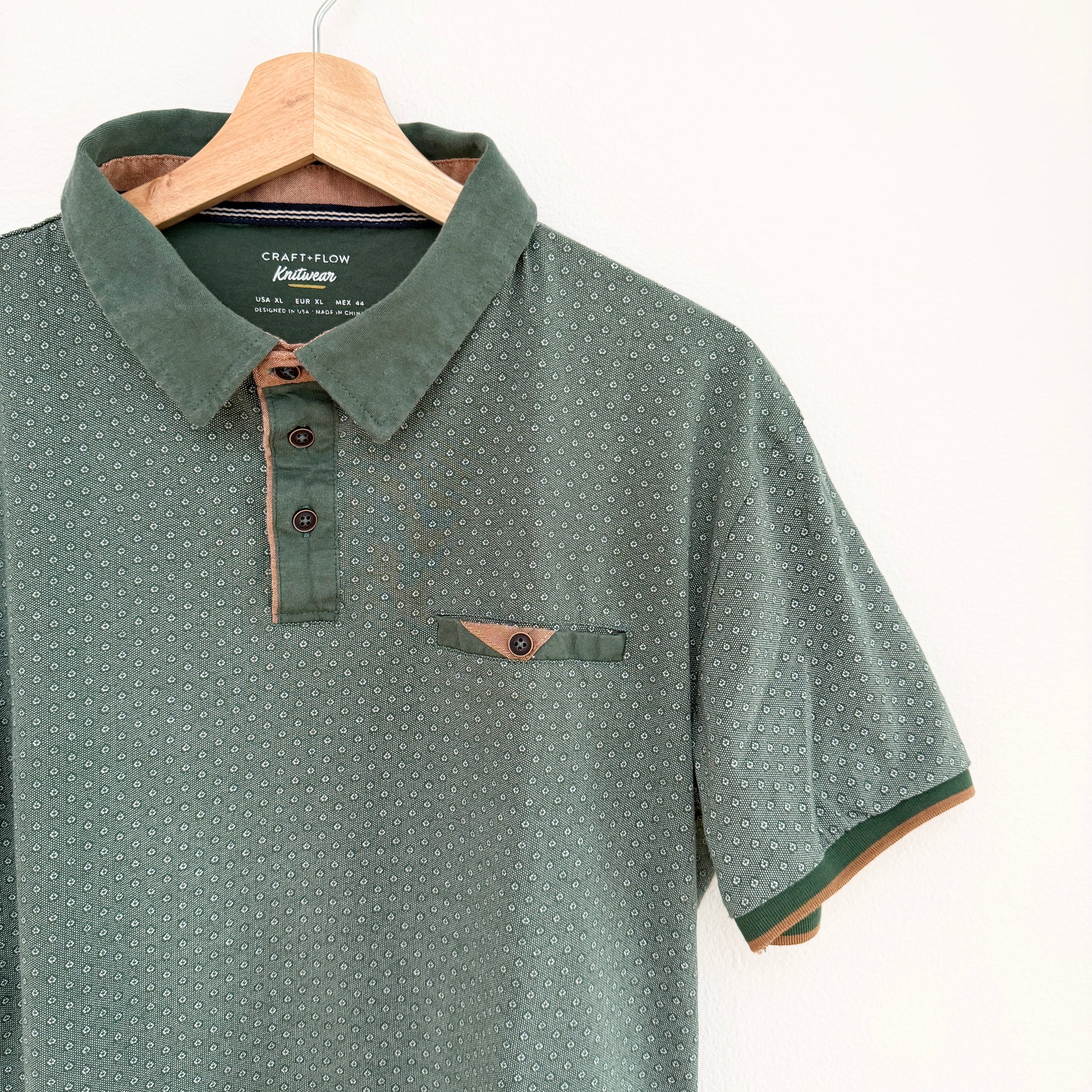 Green patterned polo shirt on a hanger with visible brand label.