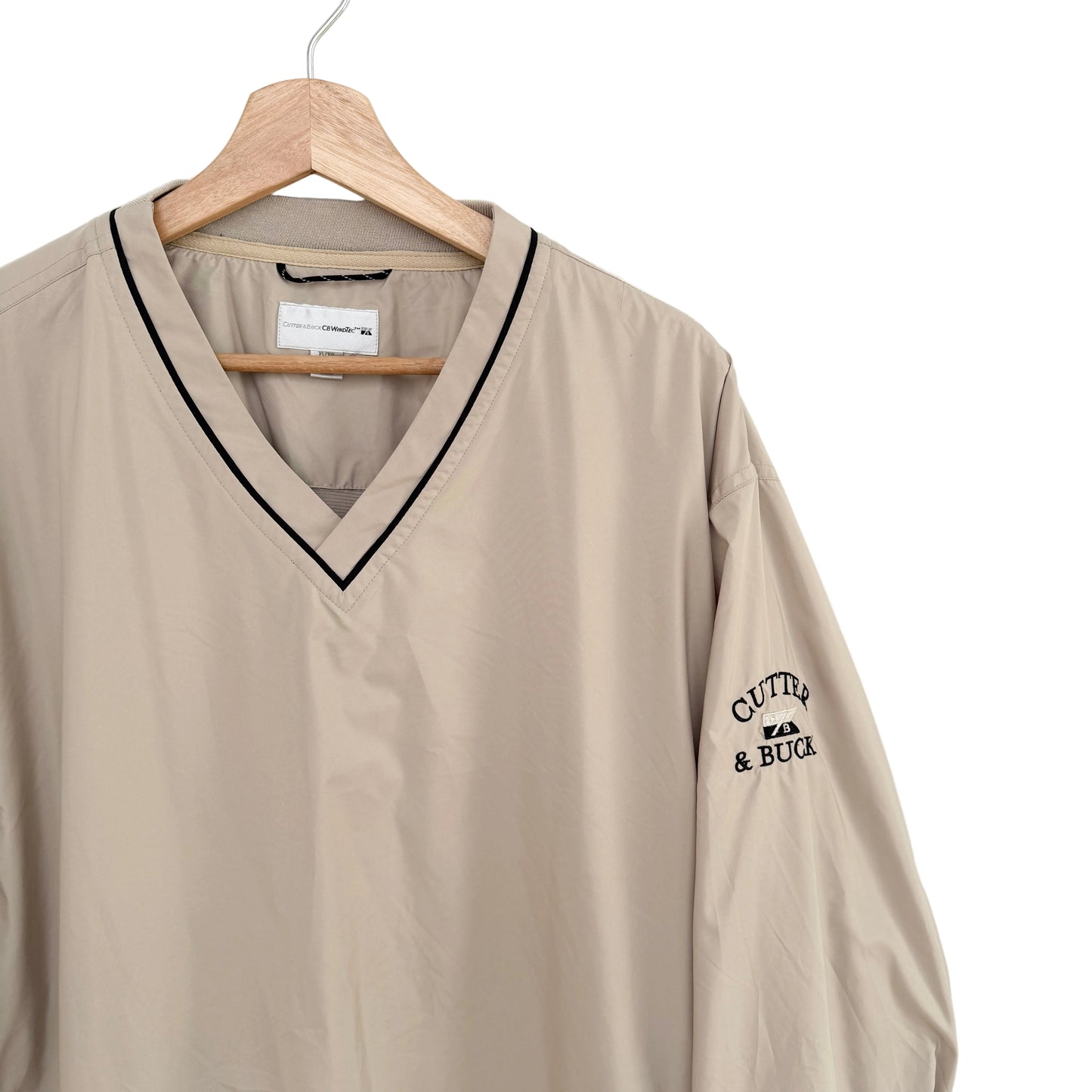 Beige shirt with black trim and 'Cutter & Buck' logo on a hanger against a white background