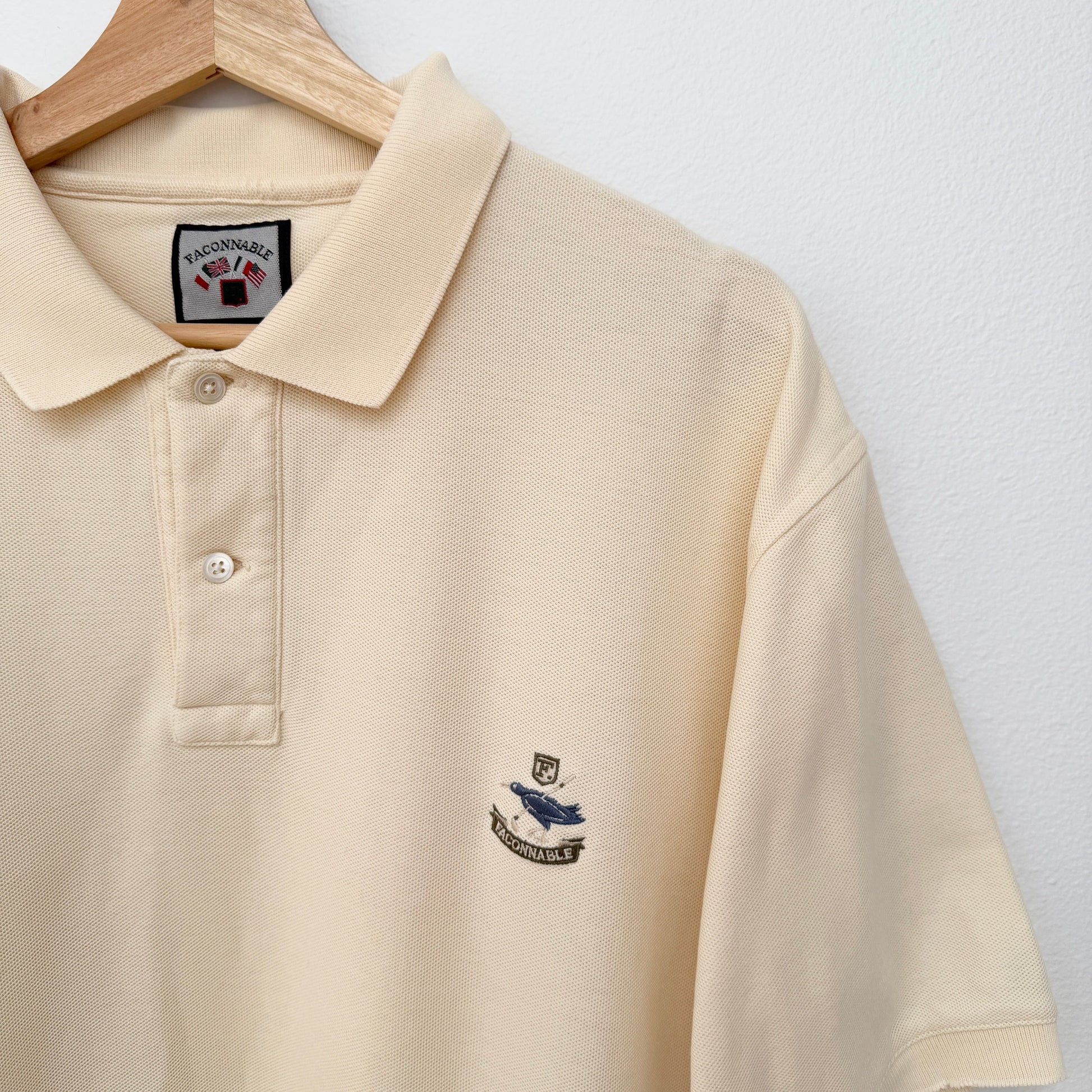 Beige polo shirt with a logo on a hanger against a white background