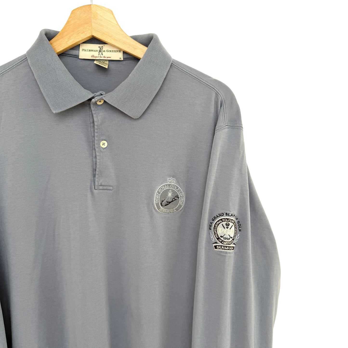 Slate blue polo shirt with embroidered logos on a beige background