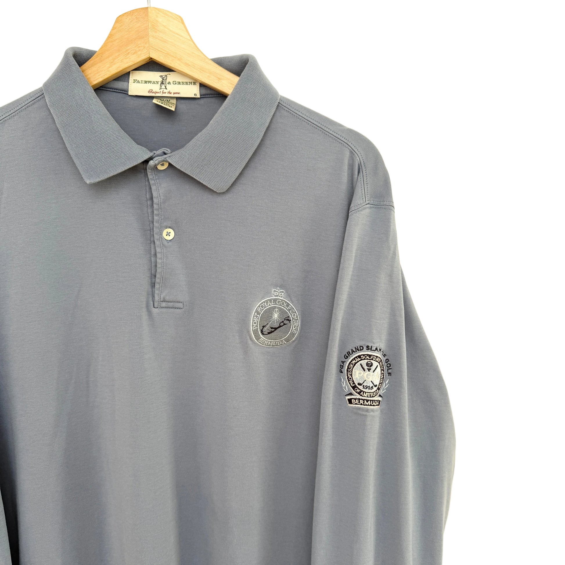 Slate blue polo shirt with embroidered logos on a beige background