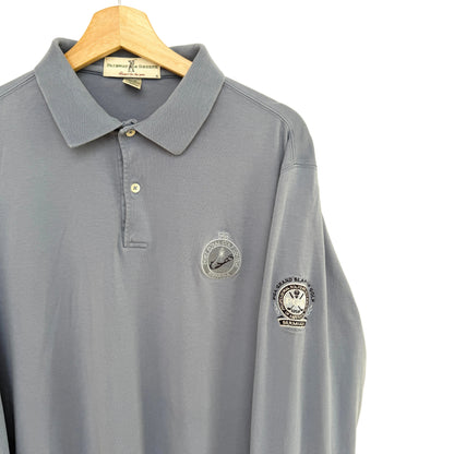 Slate blue polo shirt with embroidered logos on a beige background