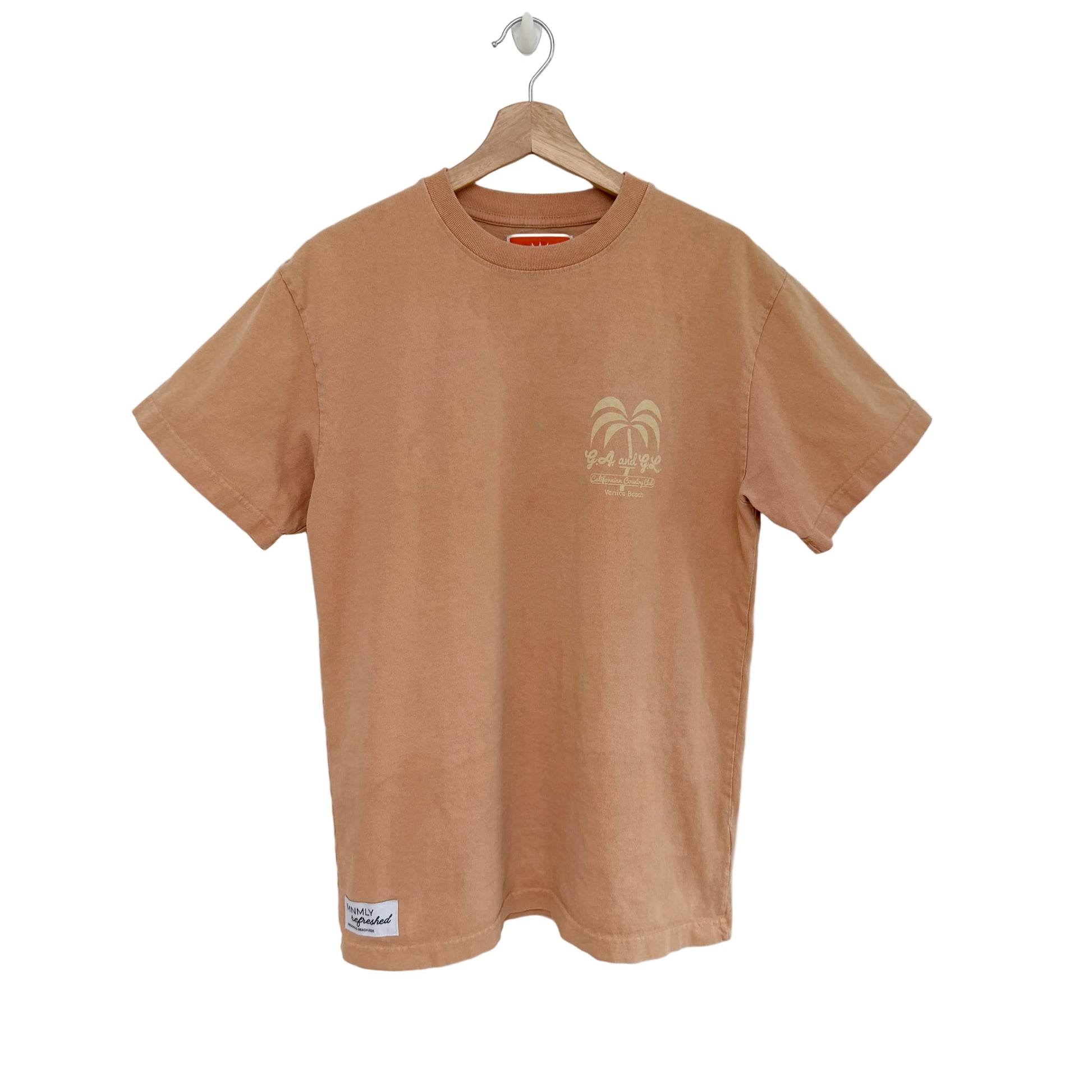 Peach t-shirt with a palm tree design on a hanger against a white background