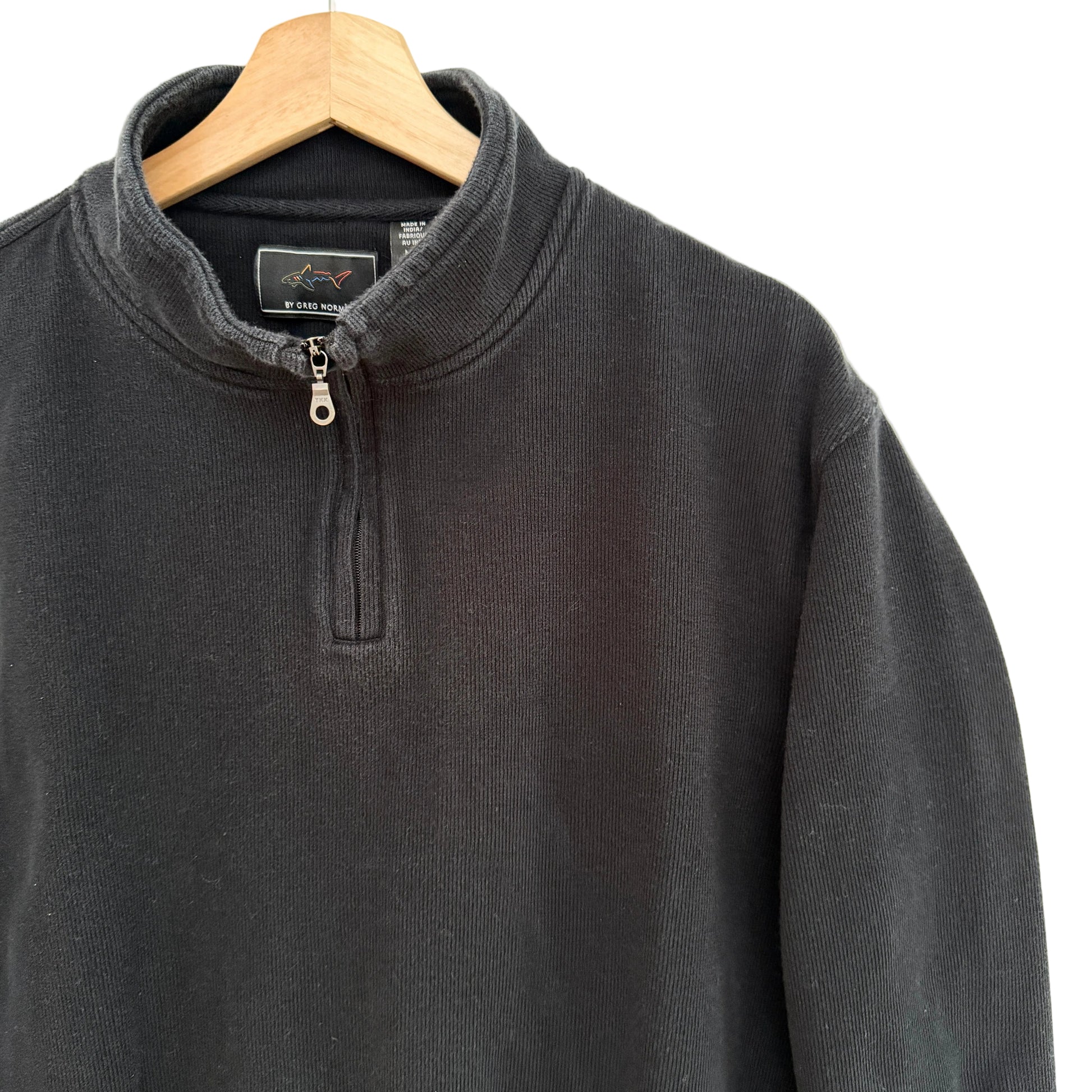 Black cotton pullover on a wooden hanger against a beige background