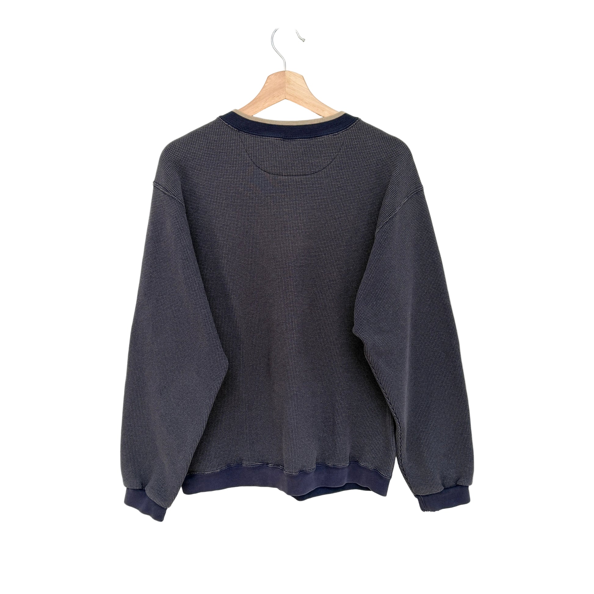 A navy crewneck sweatshirt with navy blue ribbed trim on the collar, cuffs, and hem, hanging on a wooden hanger against a plain white wall.