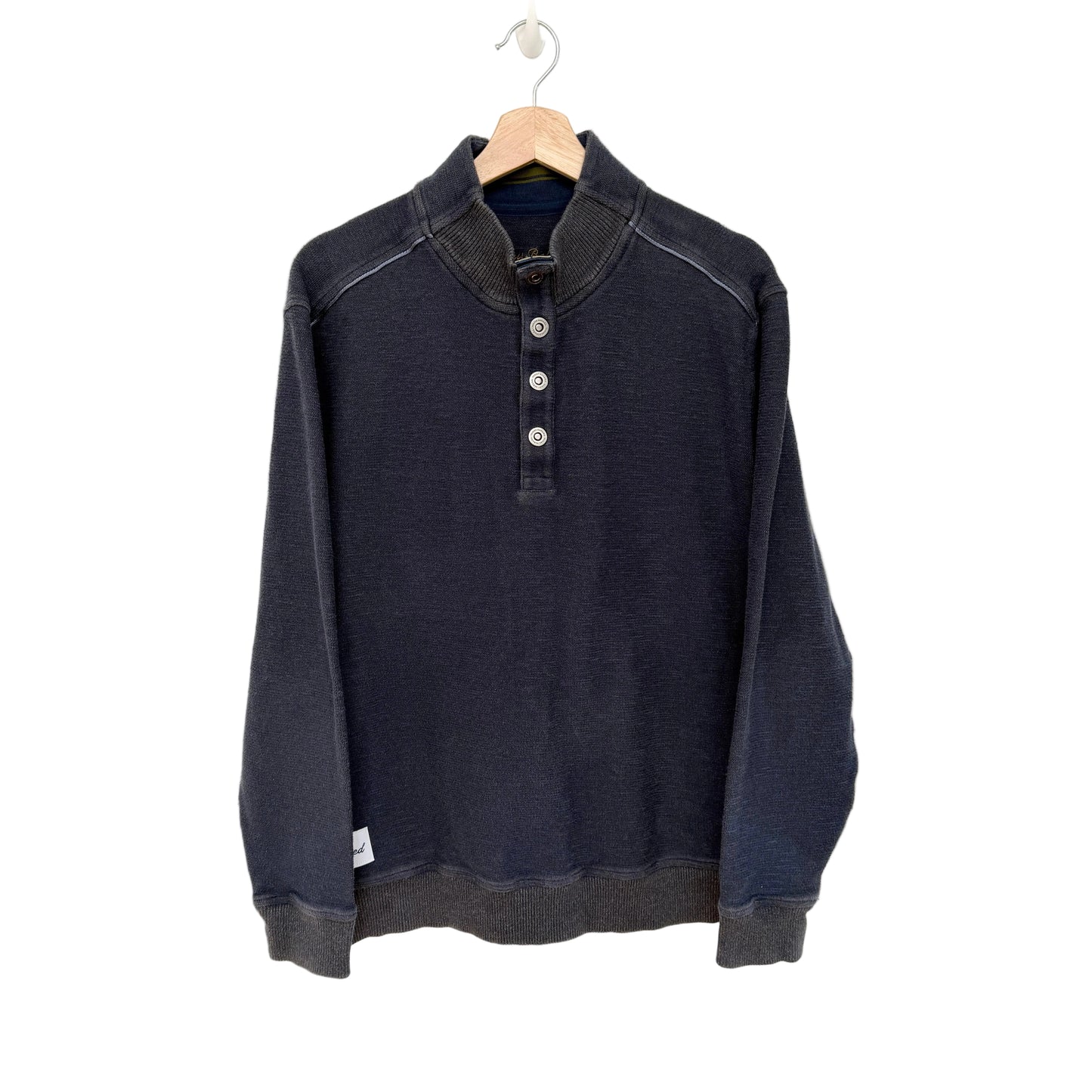 A dark navy blue long-sleeve henley shirt with a mock neck and three-button placket, hanging on a wooden hanger against a plain white wall.