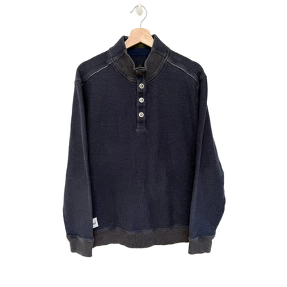 A dark navy blue long-sleeve henley shirt with a mock neck and three-button placket, hanging on a wooden hanger against a plain white wall.