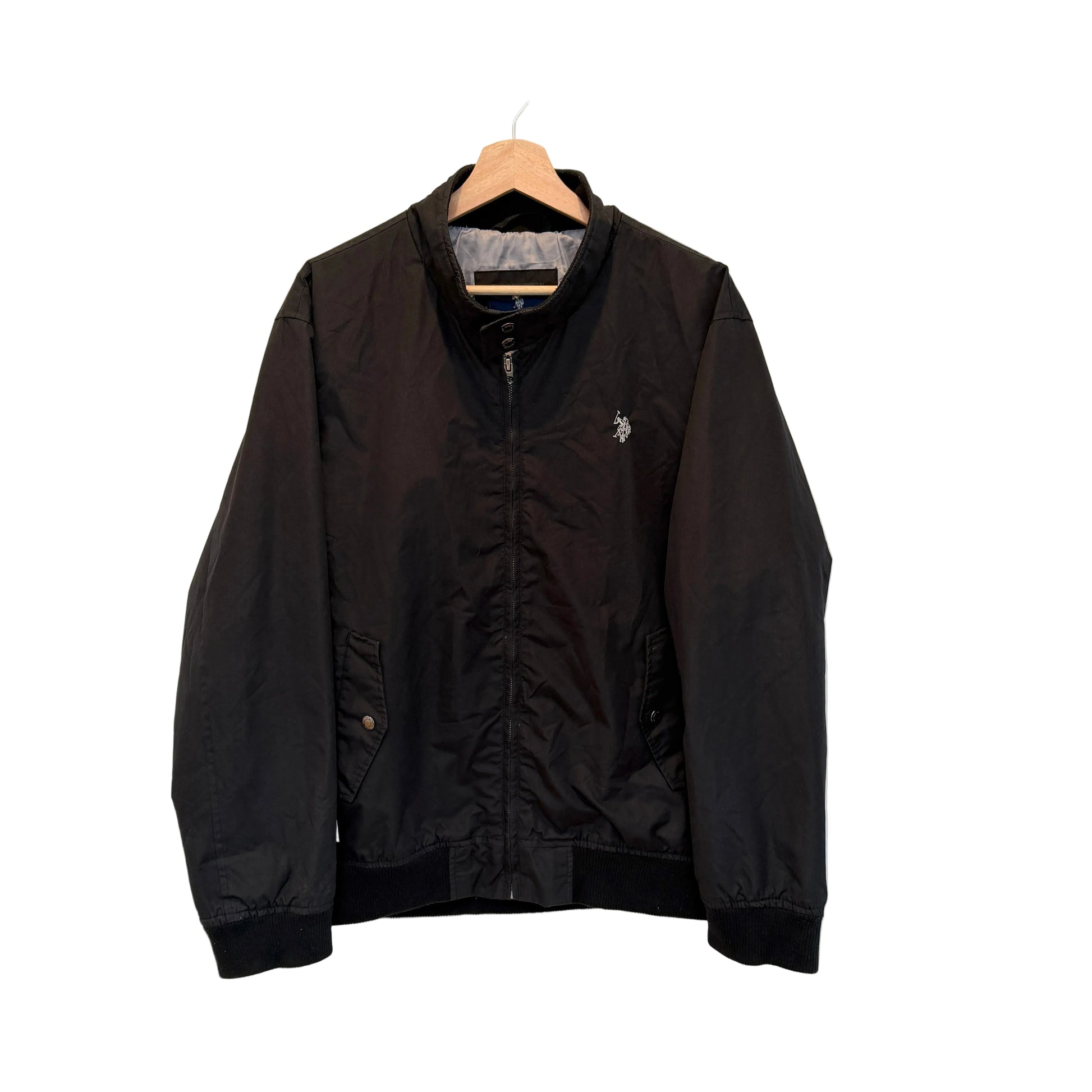 A black zip-up bomber jacket hanging on a wooden hanger against a plain white wall. The jacket features a small embroidered polo player logo on the left chest, indicating the brand Polo Ralph Lauren.