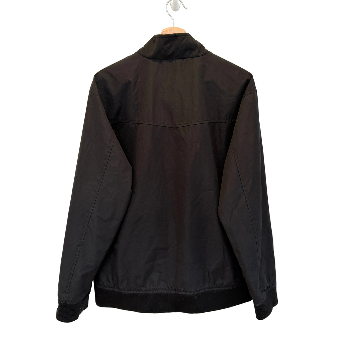 A black lightweight jacket hanging on a wooden hanger against a plain white wall, showing the back view.