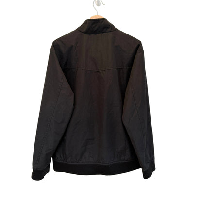 A black lightweight jacket hanging on a wooden hanger against a plain white wall, showing the back view.