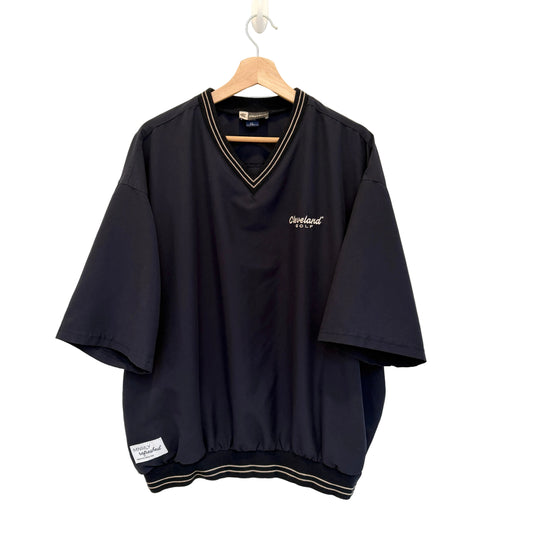 A navy short-sleeve V-neck t-shirt with gold striped trim on the collar and hem, featuring a small white embroidered 'Cleveland Browns' logo on the left chest, hanging on a wooden hanger against a white wall.