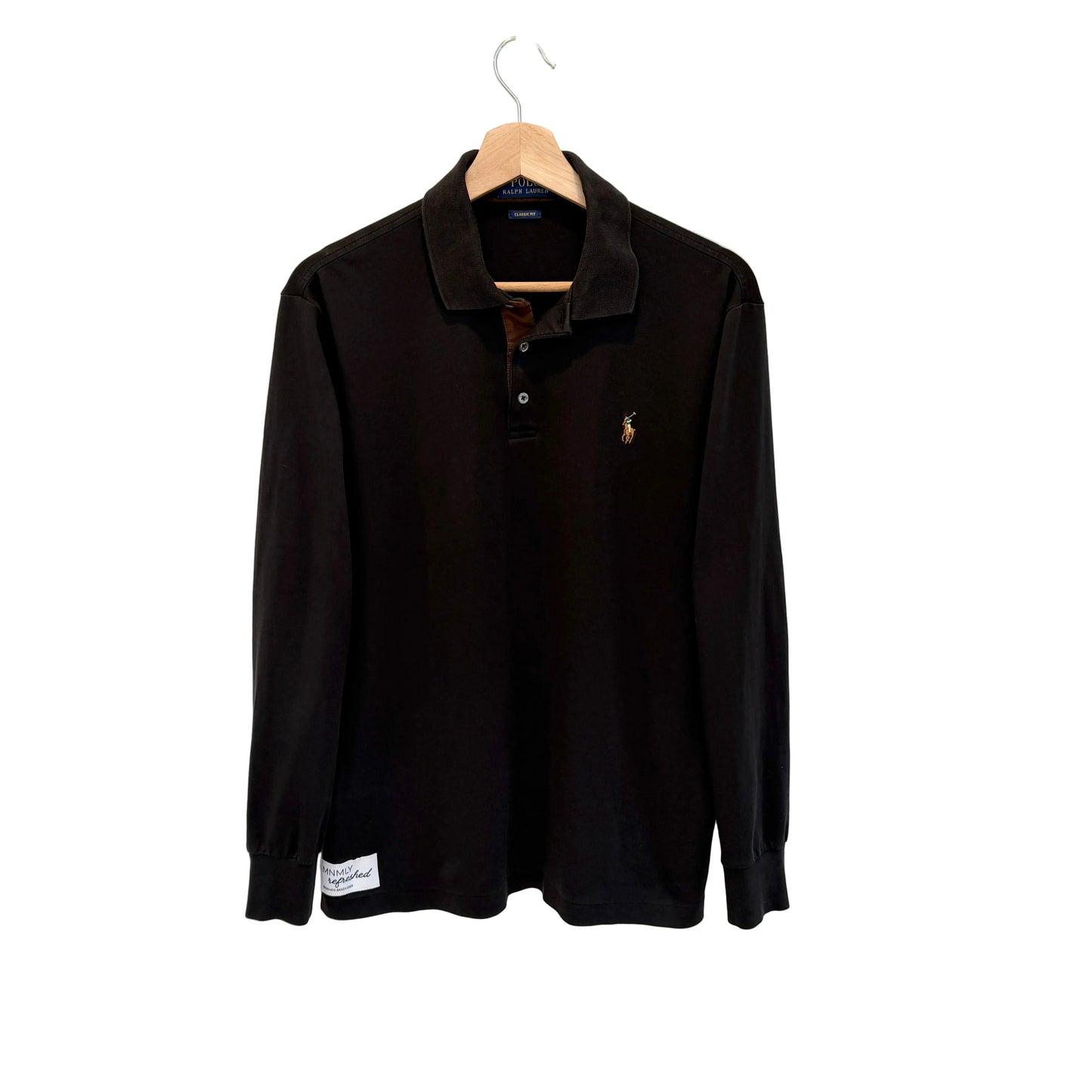 A black long-sleeve polo shirt with a small embroidered polo player logo on the left chest, hanging on a wooden hanger against a plain white wall.