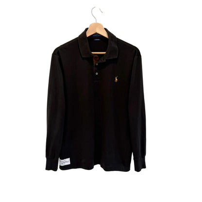 A black long-sleeve polo shirt with a small embroidered polo player logo on the left chest, hanging on a wooden hanger against a plain white wall.