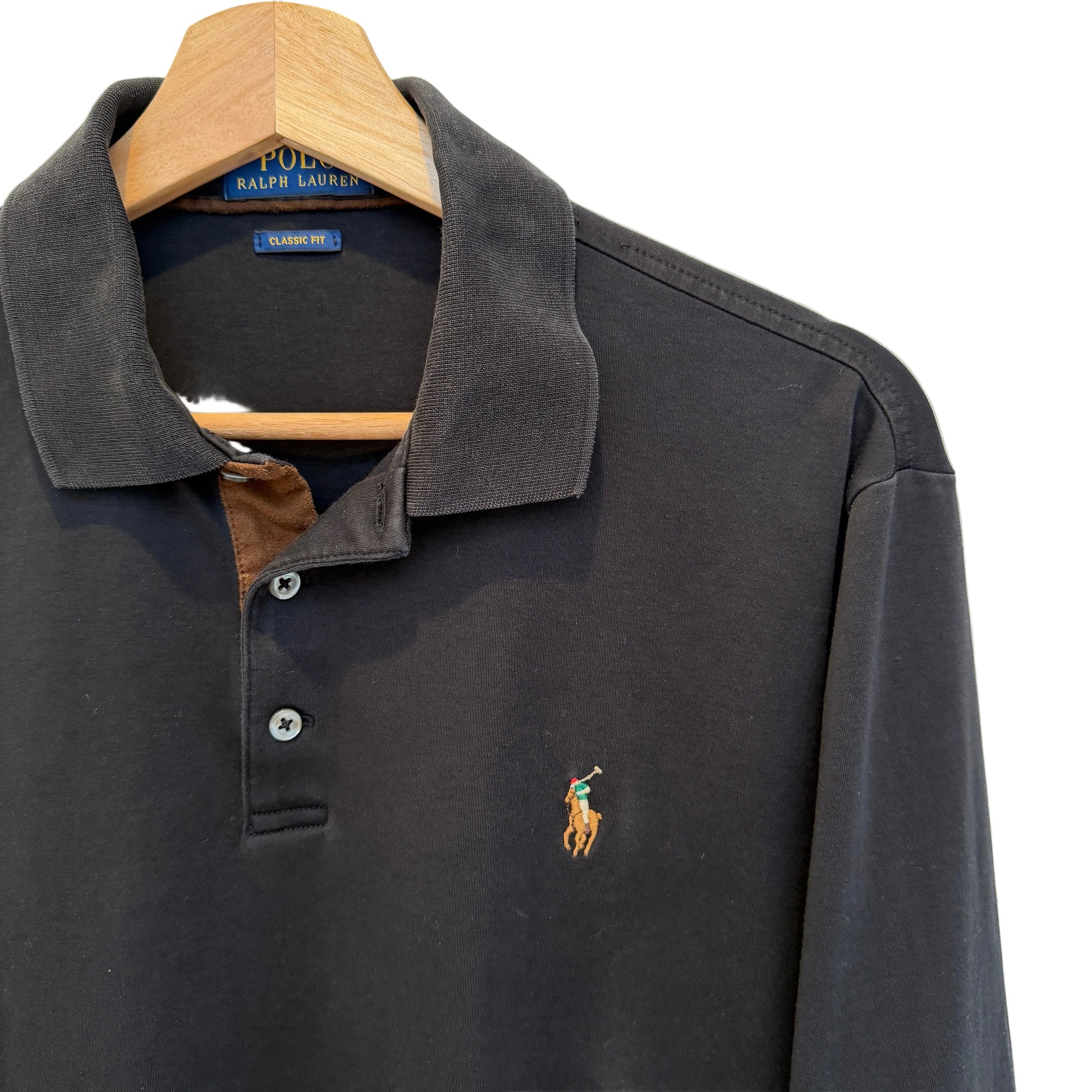 A dark charcoal gray long-sleeve polo shirt by Ralph Lauren, featuring the signature embroidered polo player logo on the left chest, hanging on a wooden hanger against a white wall.