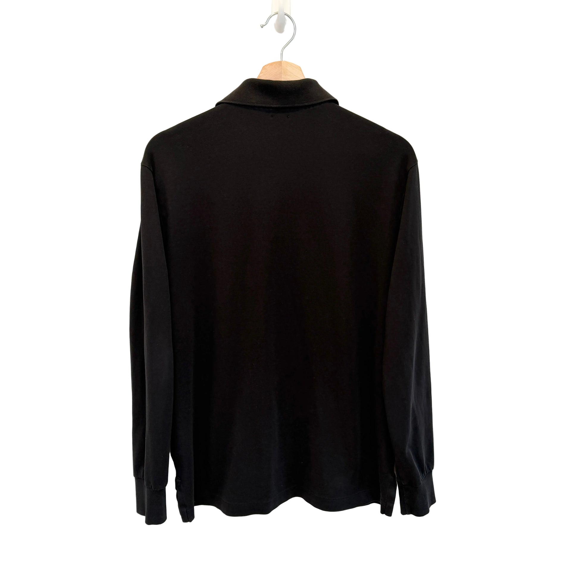 A black long-sleeve mock neck shirt hanging on a wooden hanger against a plain white wall.