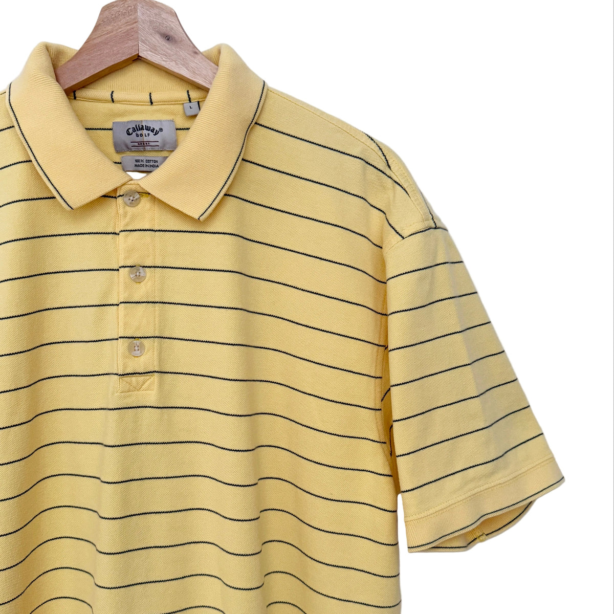 A yellow short-sleeve polo shirt with thin black horizontal stripes, hanging on a wooden hanger against a plain white wall. A small black V-neck logo is visible on the upper back.