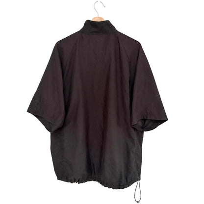 A black short-sleeve high-neck jacket or windbreaker hanging on a wooden hanger against a plain off-white wall.