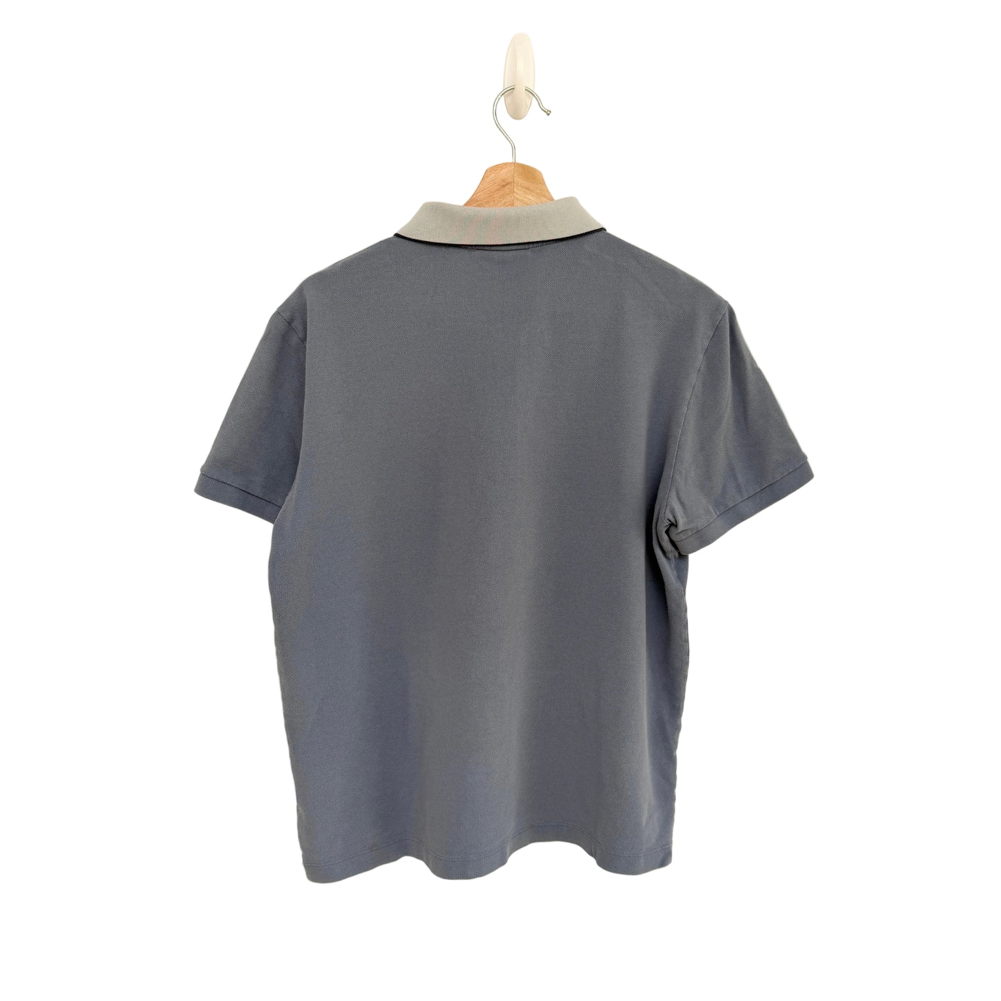 Blue polo shirt on a hanger against a beige background