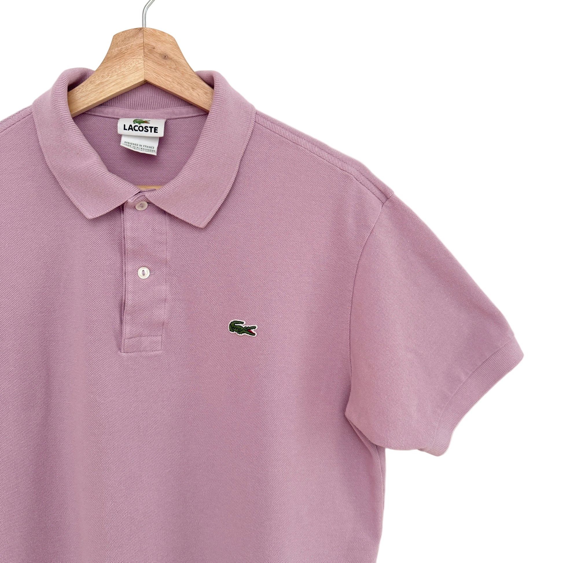 Purple polo shirt with Lacoste logo on a wooden hanger against a white background
