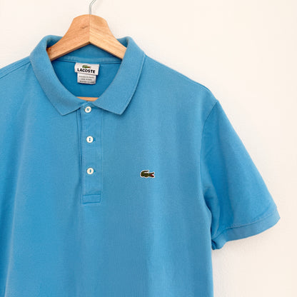 Blue polo shirt with Lacoste logo on a hanger against a white background