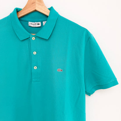 Teal polo shirt with Lacoste logo on a hanger against a white background