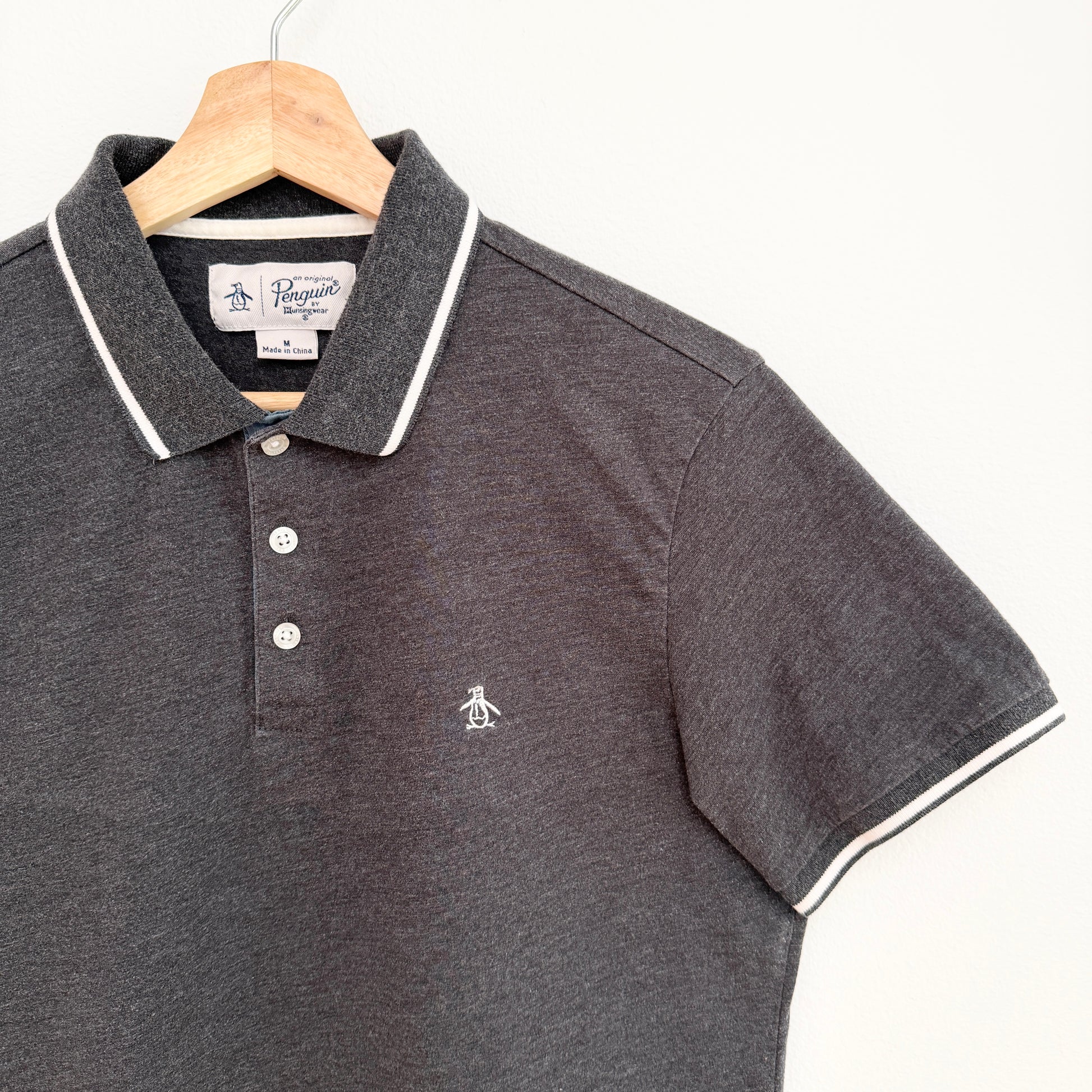 Gray polo shirt with white trim on a hanger against a white background
