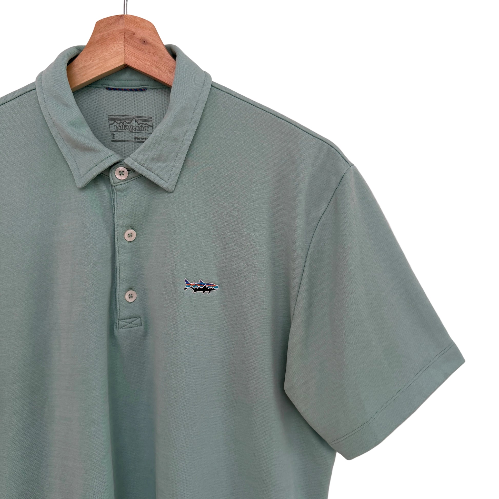 Green polo shirt with a small logo on a hanger against a light pink background