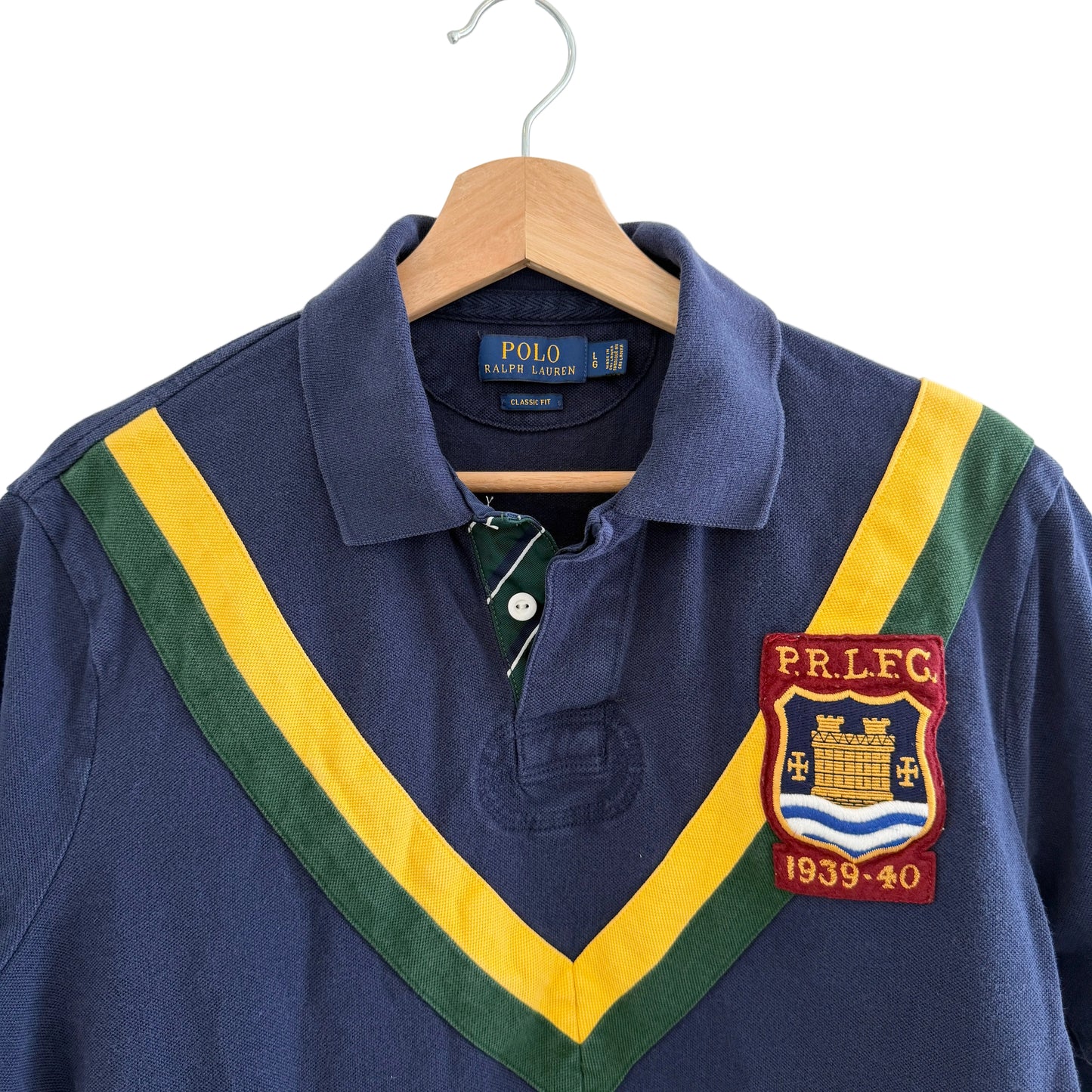 Navy blue polo shirt with colorful collar and P.R.L.F.C. patch on a hanger.