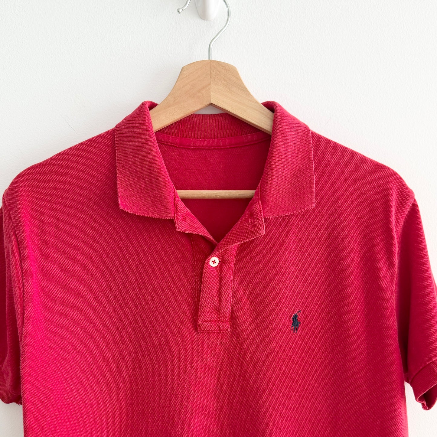 Red polo shirt with a brand logo on a wooden hanger against a white background