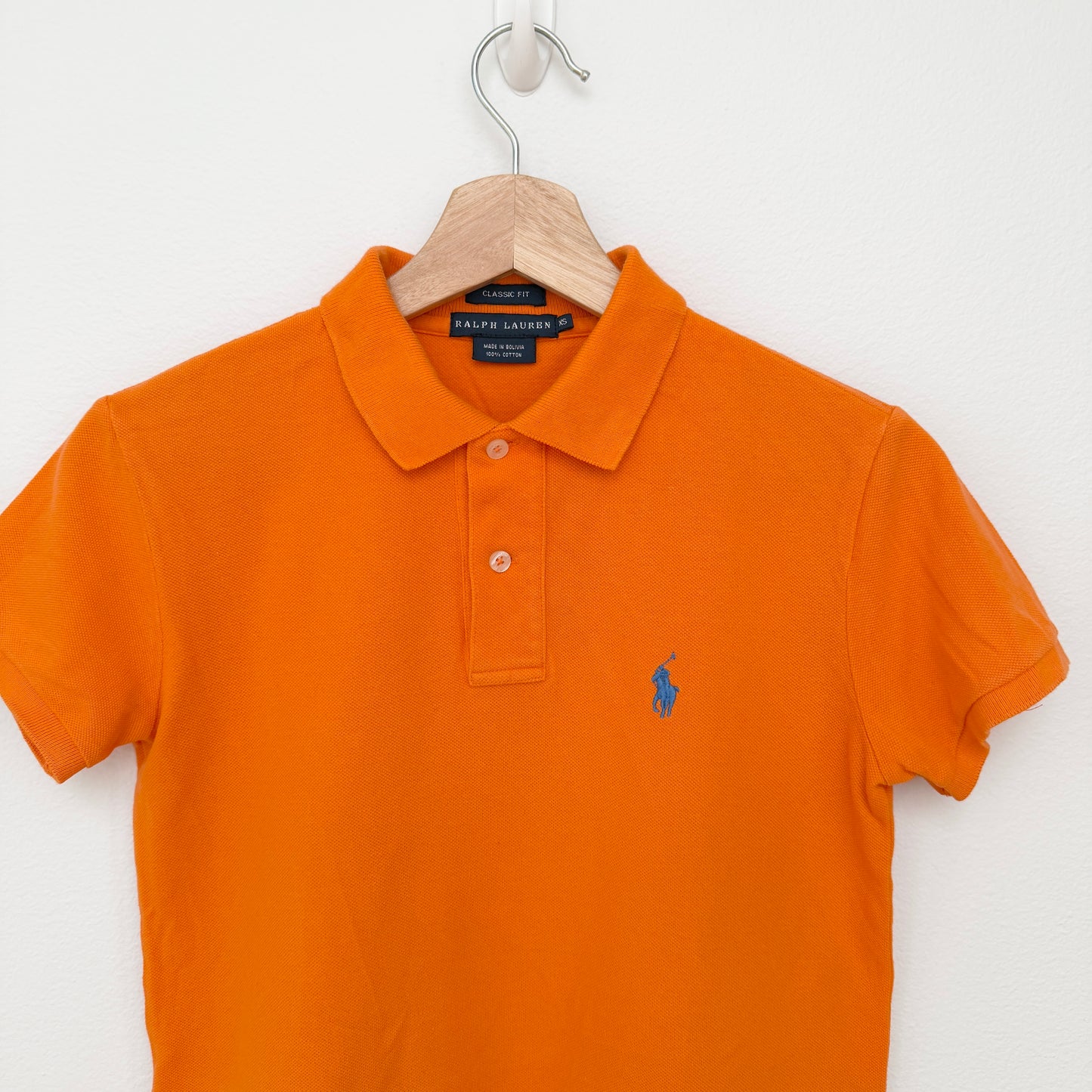 Orange polo shirt with Ralph Lauren logo on a hanger against a white background