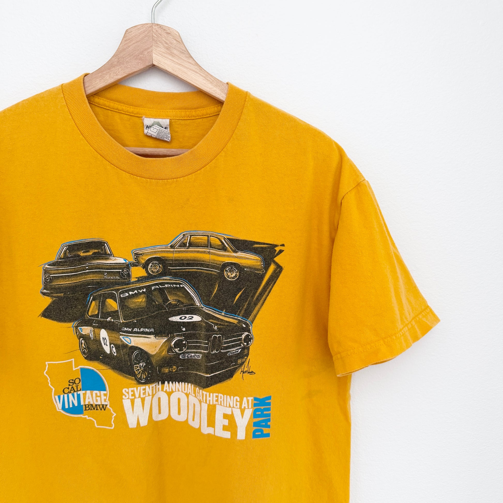 Yellow t-shirt with car graphics and text on a hanger against a white background