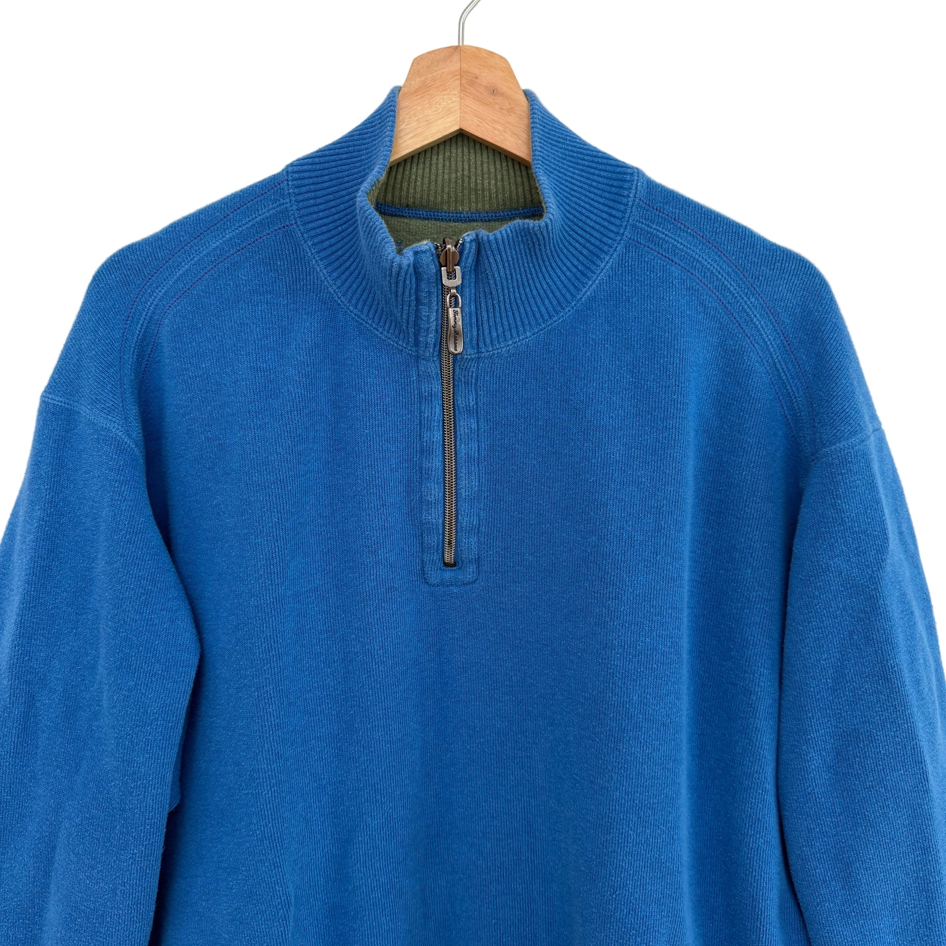 Blue sweater with a quarter zip on a wooden hanger against a white background