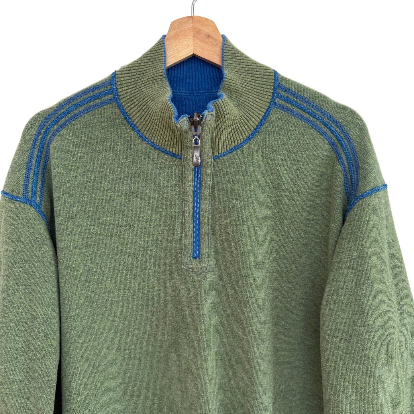 Green sweater with blue accents on a wooden hanger against a white background