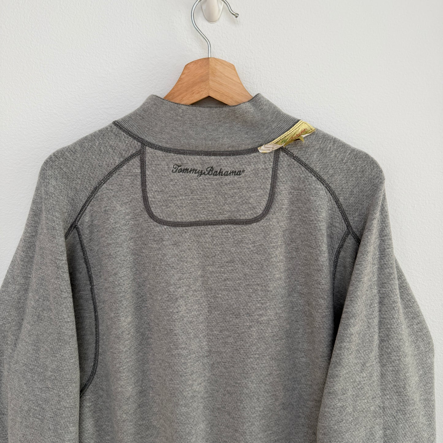 Gray fleece pullover with 'Tommy Bahama' branding on a wooden hanger against a white background