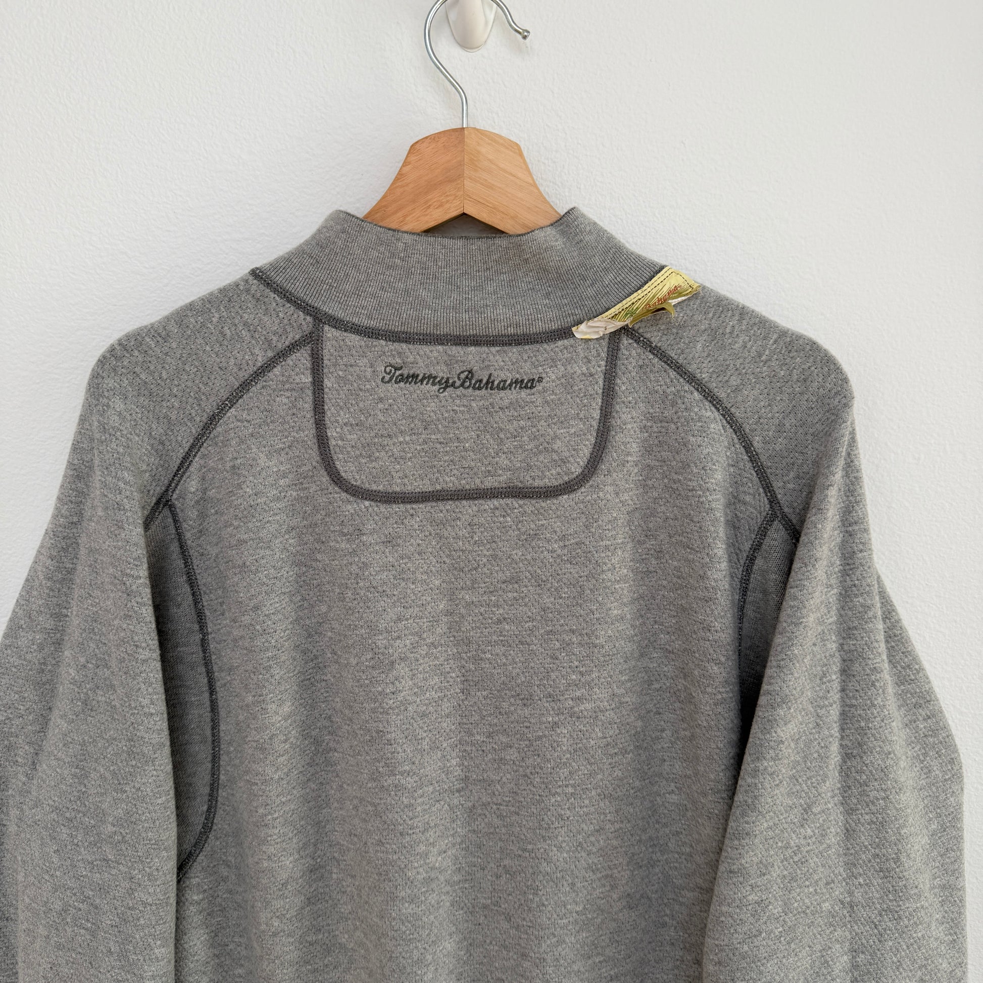 Gray fleece pullover with 'Tommy Bahama' branding on a wooden hanger against a white background