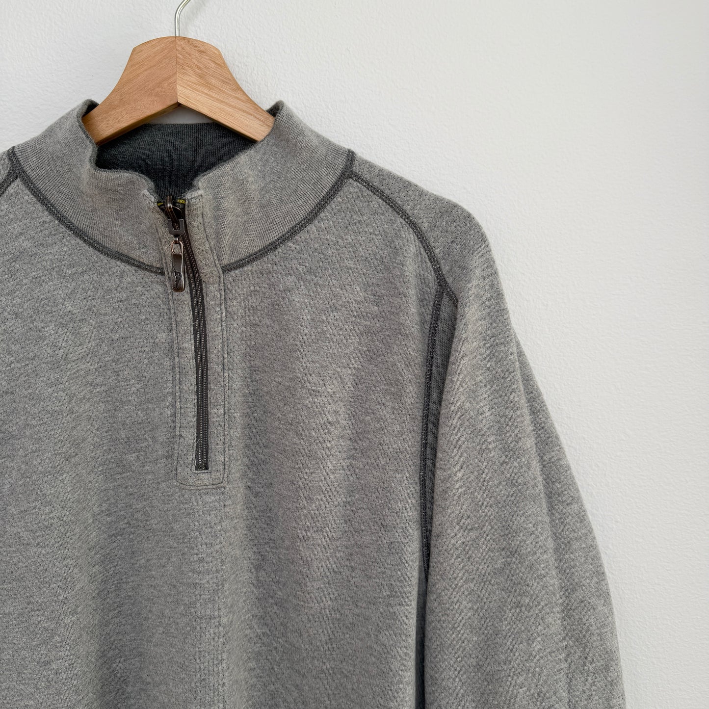 Gray pullover with a quarter zip on a wooden hanger against a white background
